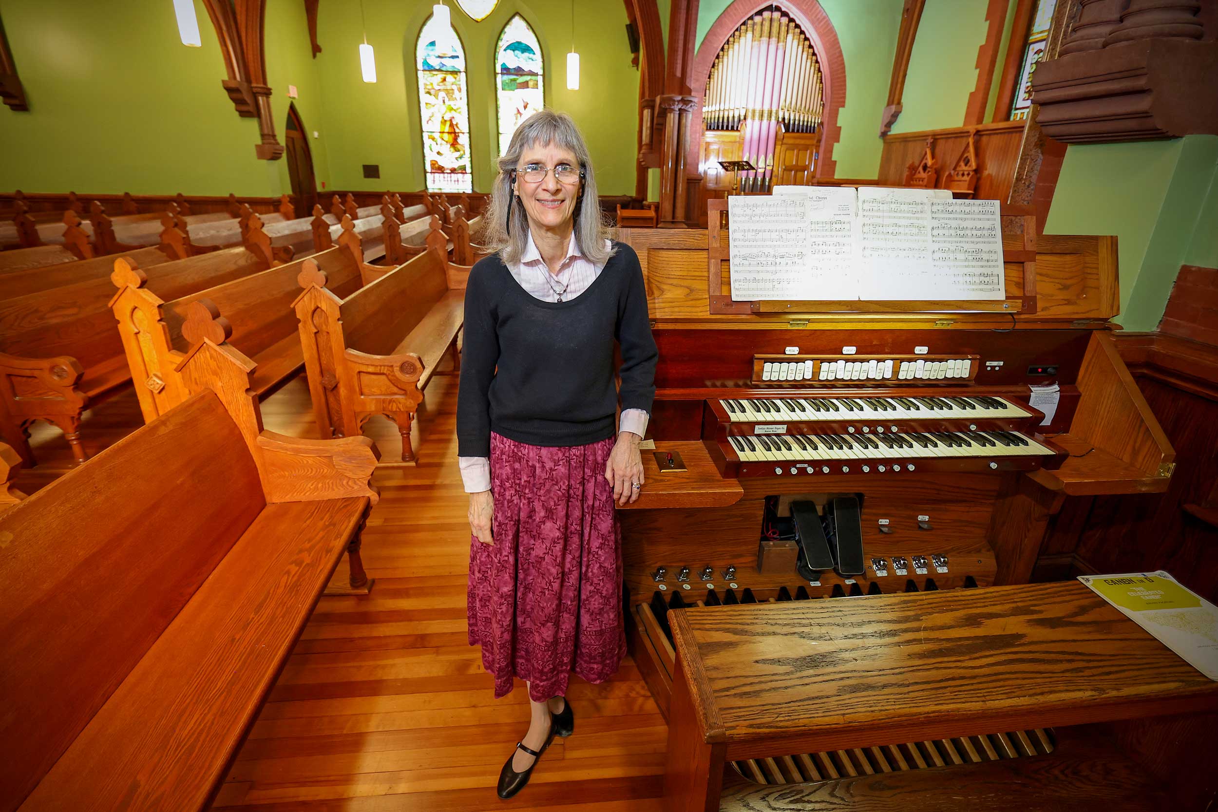 UVA Department of Music instructor Barbara Moore standing next to pipe organ keyboard console in the UVA Chapel.