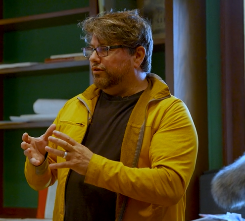 Professor Matthew Burtner wearing a yellow jacket and giving a lecture.