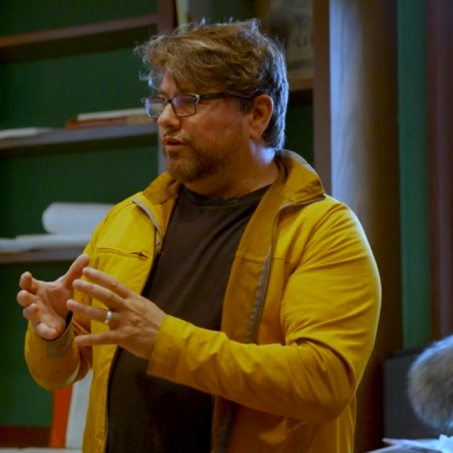 Professor Matthew Burtner wearing a yellow jacket and giving a lecture.